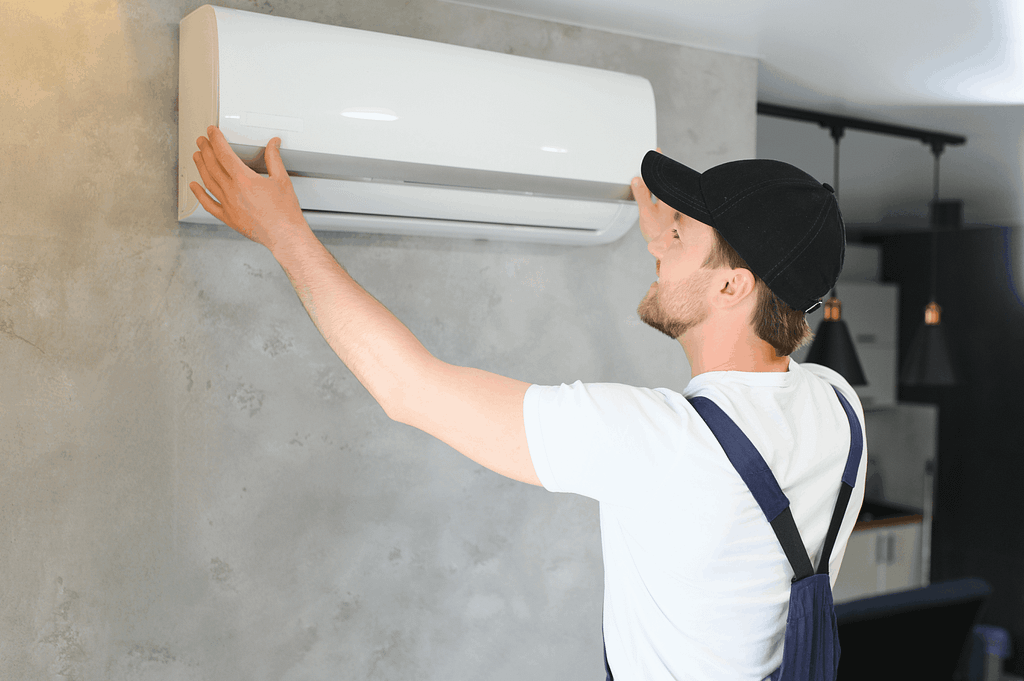 Young man installing a wall-mounted air conditioning unit in a modern home.