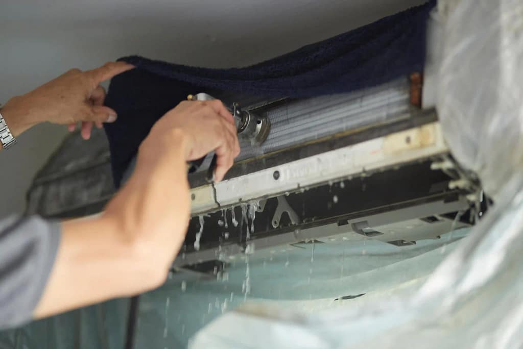 Person troubleshooting an air conditioning unit with water leaking inside.