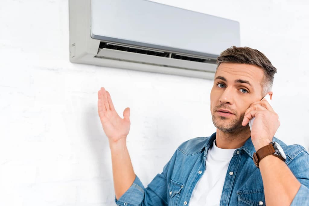 Man talking on smartphone while troubleshooting mini split air conditioner.