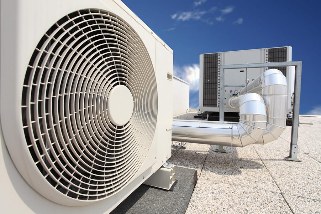 HVAC outdoor unit with fan and ductwork against a clear blue sky