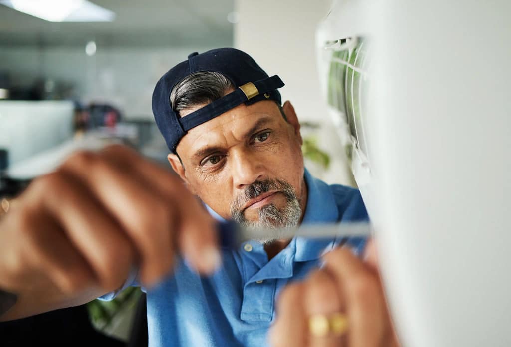 Man repairing an air conditioner in an office setting, focusing on HVAC maintenance.